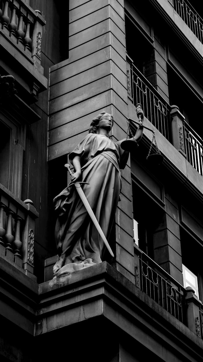 A dramatic black and white photo of a justice statue holding a sword and scales.